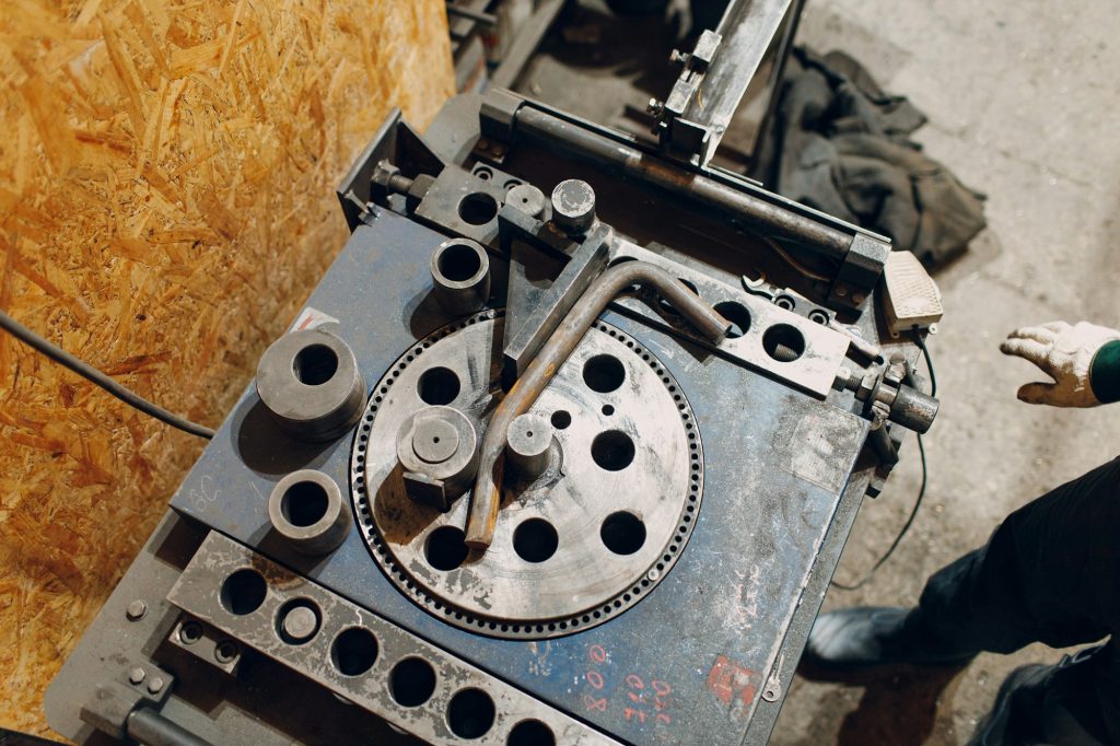 Worker at factory with industrial machine for bending of metal pipes